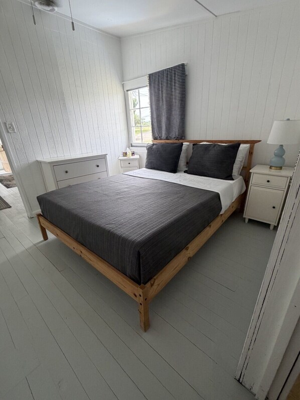 A bedroom with a large bed, a nightstand, a bedside table, a window with blinds, and a ceiling fan. - Plum Point Cottage #17 (Huntingtown)