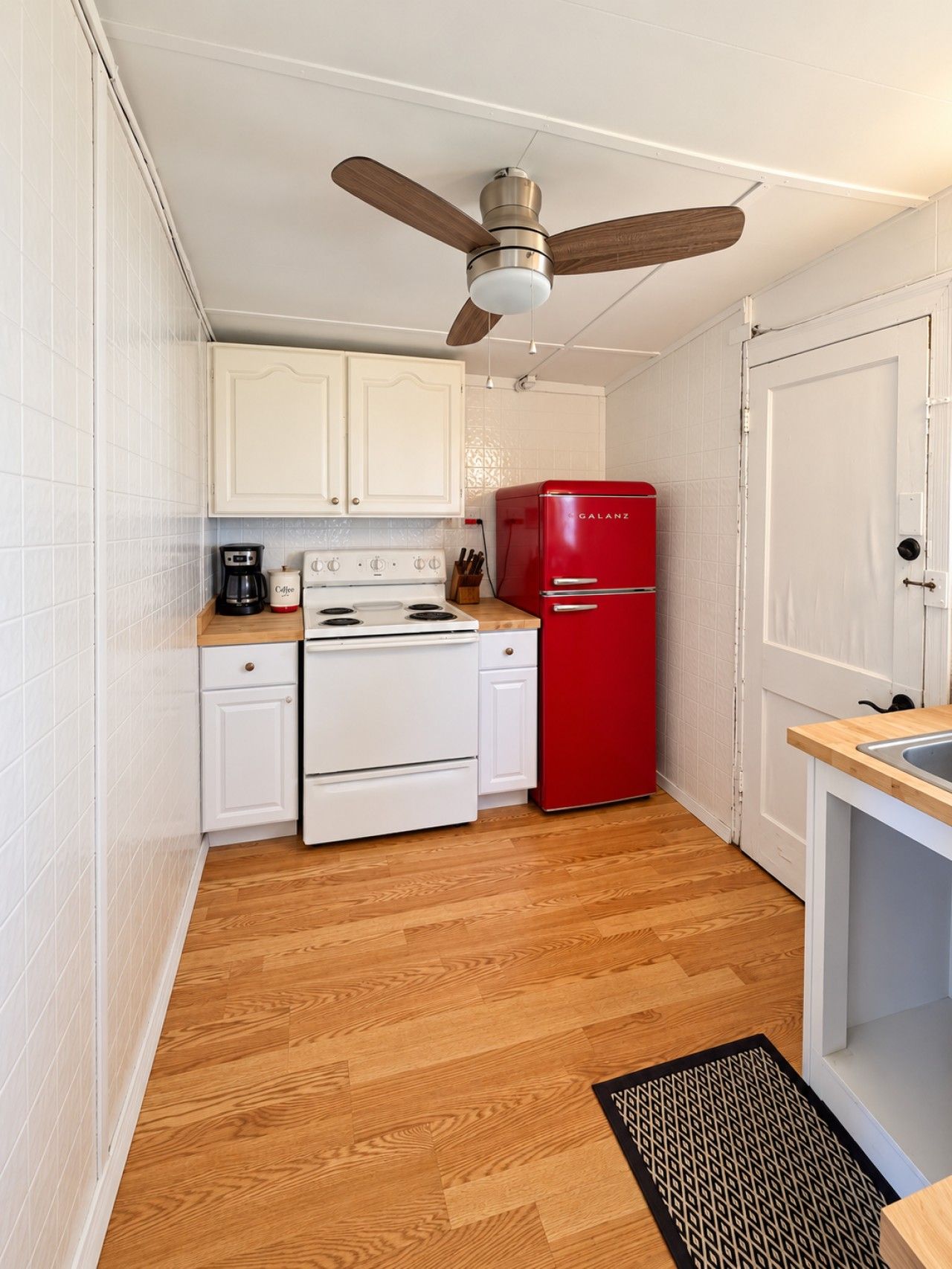A compact kitchen with white cabinets, a red refrigerator, a stove, and a ceiling fan.