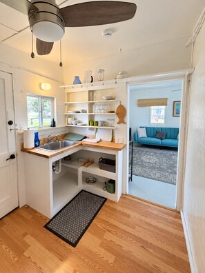 A compact kitchen with a built-in sink, wooden countertop, and a ceiling fan.