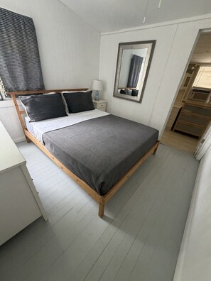 A bed with a wooden frame, a bedside table with a lamp, and a mirror on the wall. - Plum Point Cottage #17 (Huntingtown)