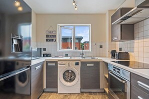 Eine kompakte Küche mit Waschmaschine, Spüle und Fenster mit Blick auf Gebäude.