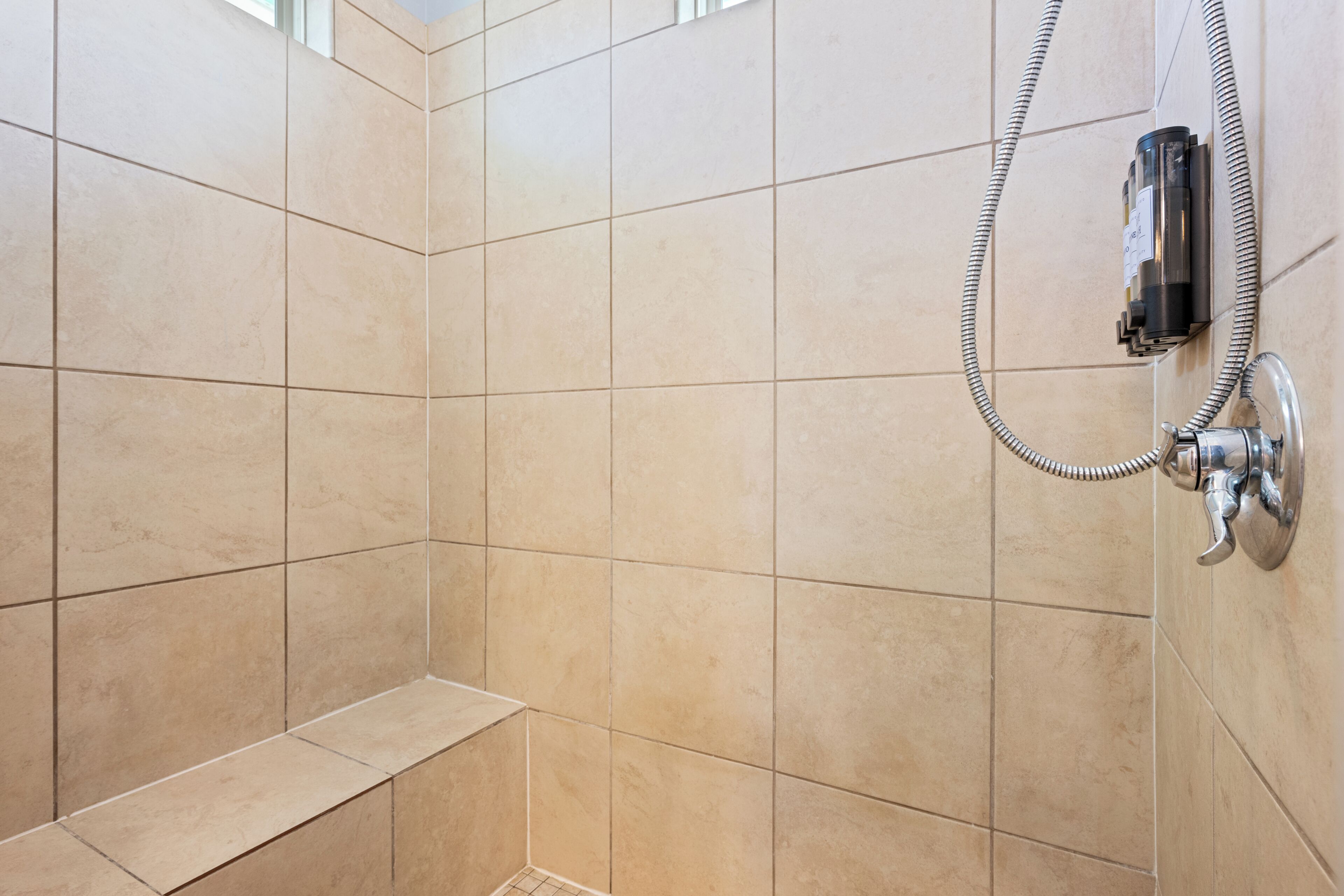 A tiled shower area with a handheld showerhead and a wall-mounted faucet.