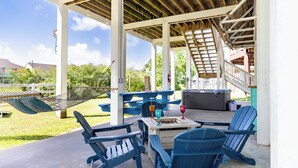 A covered outdoor seating area with Adirondack chairs, a table, and a grill. - Crystal Beach Oasis, Hot Tub, 2 Decks, 2 Main Suites, Walk to the Beach, Dogs (Bolivar Peninsula)