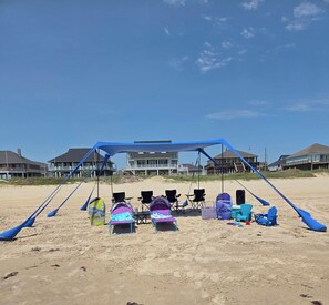 Ein Strand mit einer blauen Sonnensegelkonstruktion, Liegestühlen und einem Lautsprecher.