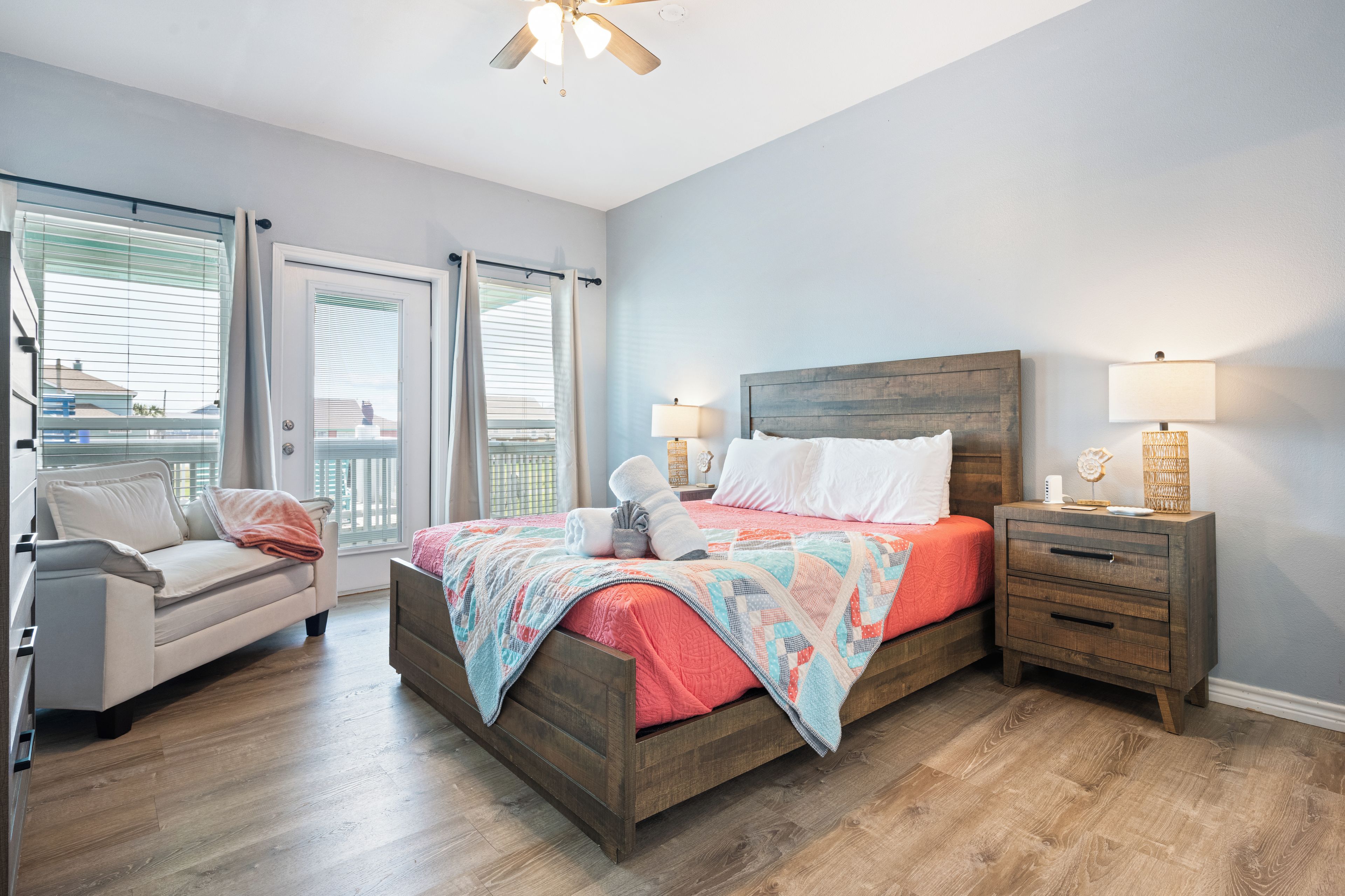 A bedroom with a wooden bed, a nightstand with a lamp, a window with blinds, and a view of the outside.