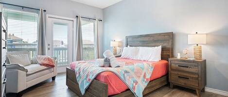 A bedroom with a wooden bed, a nightstand with a lamp, a window with blinds, and a view of the outside.