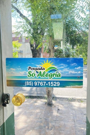 Uma placa com uma cena de praia, o nome 'Pousada So Alegre' e um número de telefone.