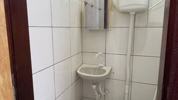 Un baño pequeño con azulejos, que incluye un inodoro, un lavamanos y un dispensador de papel higiénico en la pared.