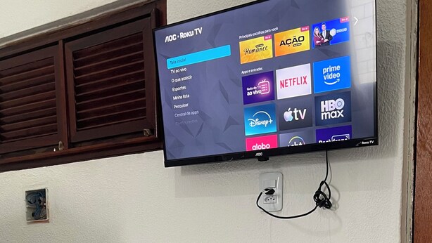 Televisão de tela plana fixada na parede, exibindo diversos serviços de streaming.