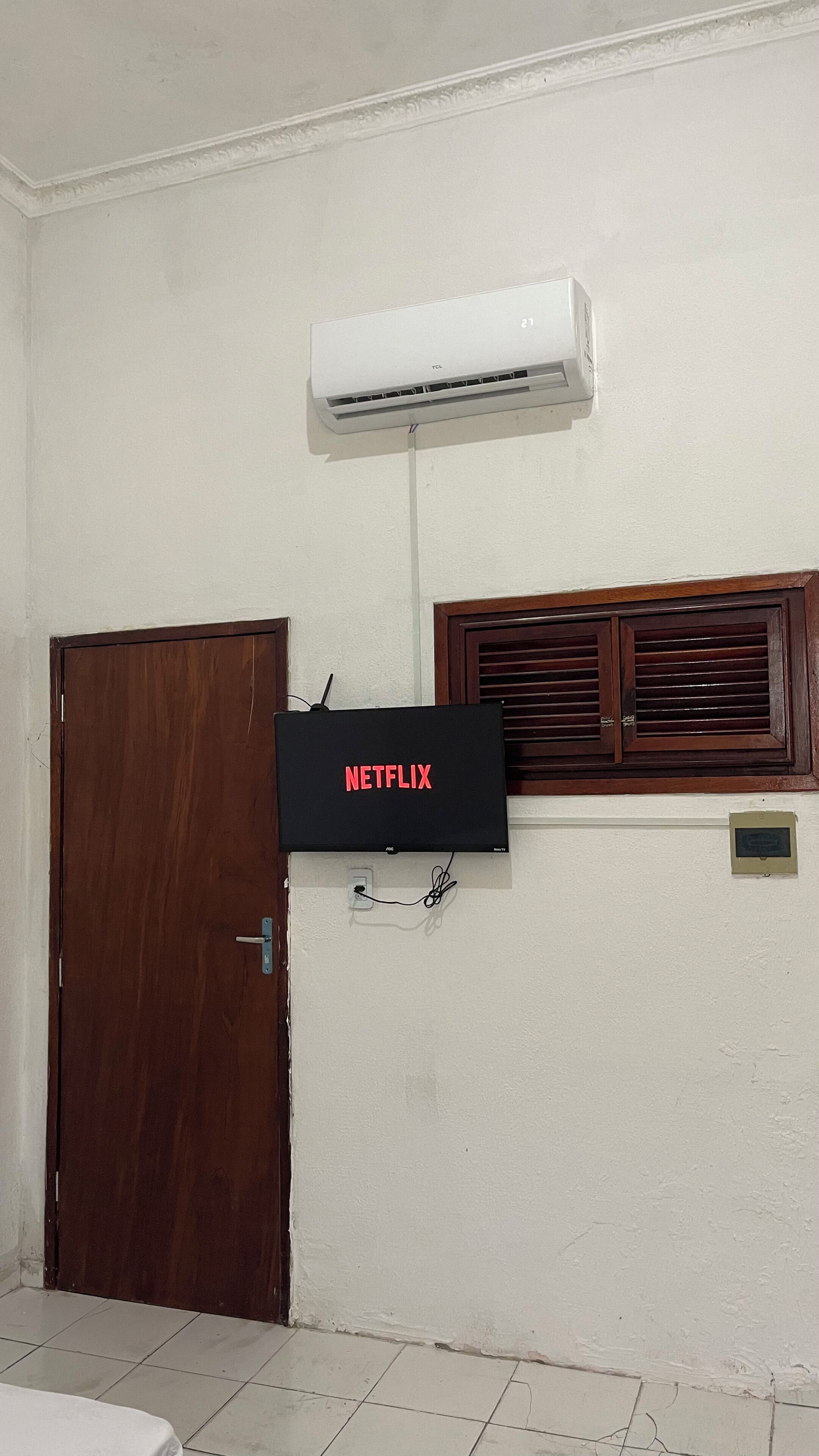 A room with a wooden door, a wall-mounted air conditioner, and a television displaying 'NETFLIX'.