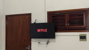 A room with a wooden door, a wall-mounted air conditioner, and a television displaying 'NETFLIX'.