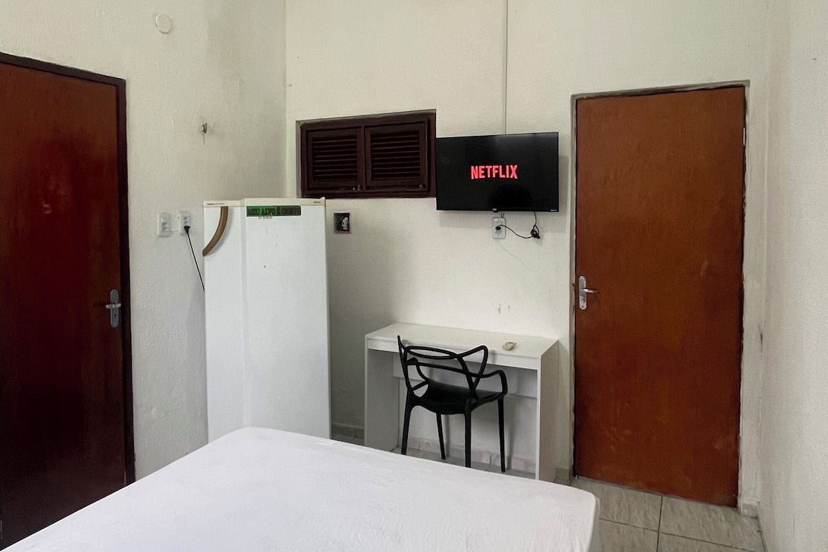 A hotel room with a bed, a desk with a chair, a TV, and an air conditioning unit.