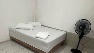 A room with a bed, a standing fan, and a patterned rug.