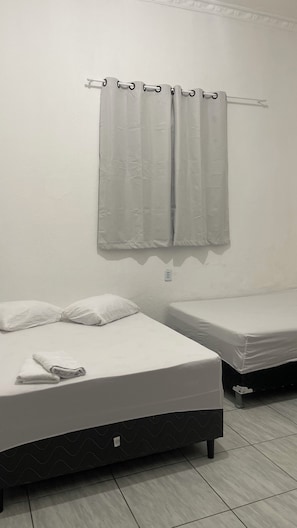 Quarto com duas camas, cortina e tomada.