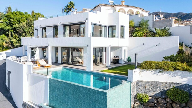 Et moderne hus med to etager, en swimmingpool, store vinduer og udsigt over det omkringliggende landskab.