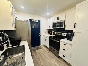 A modern kitchen with white cabinets, a blue door, stainless steel appliances, and a coffee station.