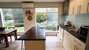 A modern kitchen with a central island, large windows, and a view of greenery.