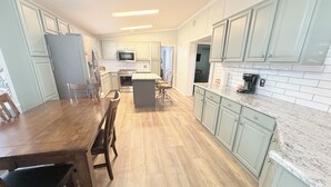 Une cuisine avec des meubles de couleur vert clair, une table à manger en bois et un îlot central.