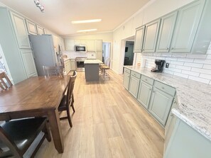 Eine Küche mit hellgrünen Schränken, einem Holztisch und einer zentralen Kochinsel.