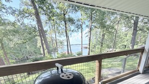 Un espace extérieur abrité, doté d’un barbecue, d’une rambarde en bois et offrant une vue sur un lac et des arbres.