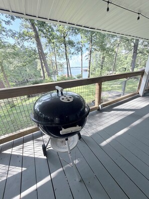Ein überdachter Außenbereich mit Grill, Holzgeländer und Blick auf See und Bäume.