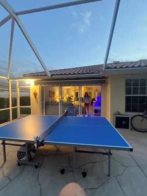 A ping pong table in an outdoor area with a glass enclosure, a bicycle, and a house in the background. - Sarasota Paradise in VillageWalk 2 Pools, Tennis, Pickleball, Fitness & Dining (Sarasota)