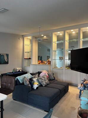 A living room with a sofa, a television, and a dining area with a table and chairs. - Sarasota Paradise in VillageWalk 2 Pools, Tennis, Pickleball, Fitness & Dining (Sarasota)