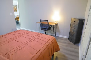 Ein Schlafzimmer mit einem Bett, einem Schreibtisch, einem Stuhl, einer Lampe und einem Aktenschrank.