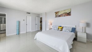 A modern bedroom with a large bed, a nightstand, a lamp, a painting, and a door leading to a bathroom. - New  Beach view Paradise (Hollywood)