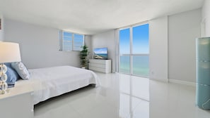 A modern bedroom with a large bed, a TV, and a view of the ocean. - New  Beach view Paradise (Hollywood)