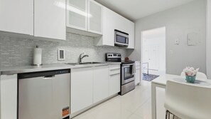 A modern kitchen with white cabinets, a stainless steel dishwasher, a built-in oven, and a microwave. - New  Beach view Paradise (Hollywood)