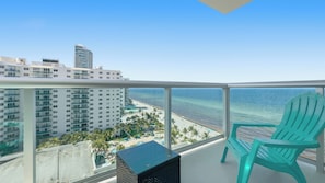 A balcony with a view of the ocean, a turquoise chair, and a pool area with palm trees. - New  Beach view Paradise (Hollywood)