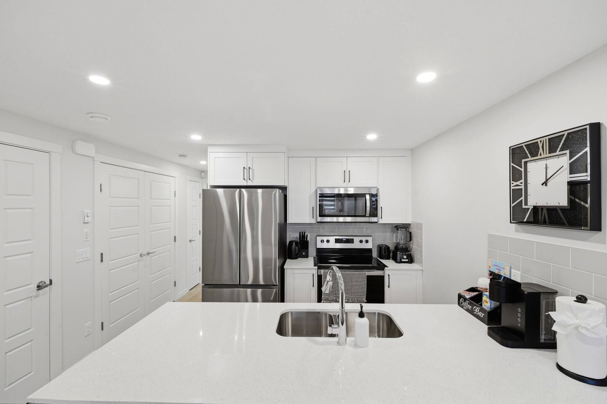 Una cocina moderna con armarios blancos, electrodomésticos de acero inoxidable, una cafetera y un reloj en la pared.