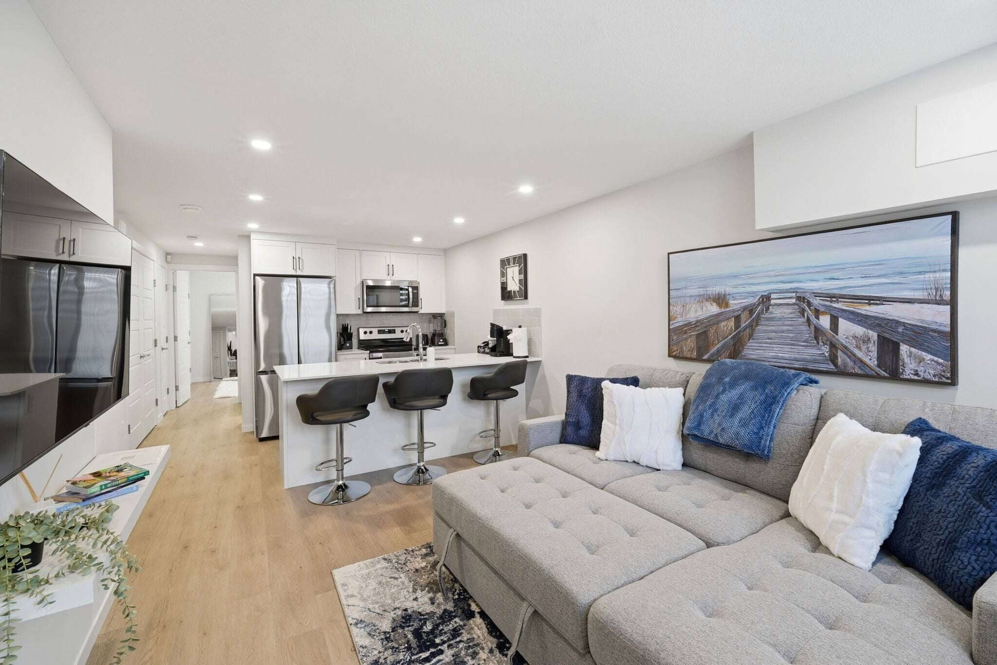 A modern apartment with a kitchenette, a dining area, a living room with a sofa, and a large window with a view.