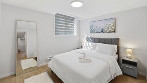 Um quarto moderno com uma cama grande, mesa de cabeceira com abajur, espelho e janela com persianas.