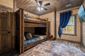 Ein rustikales Holzhäuschen im Inneren, mit einem Stockbett, einem runden Tisch und einem Deckenventilator.