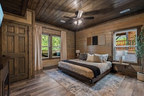 A wooden cabin bedroom with a bed, ceiling fan, and large windows. - Midnight in the Smokies, Sleeps 32, Pool, Hot Tub, Game Room with Arcade (Sevierville)