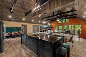 A spacious kitchen with a large island, wooden ceiling beams, and a dining area with chairs and a table. - Midnight in the Smokies, Sleeps 32, Pool, Hot Tub, Game Room with Arcade (Sevierville)