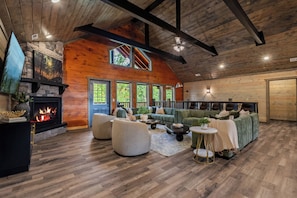 A spacious living room with a fireplace, large windows, and a high ceiling. - Midnight in the Smokies, Sleeps 32, Pool, Hot Tub, Game Room with Arcade (Sevierville)