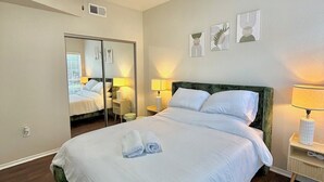 Une chambre d’hôtel avec un lit, un ventilateur de plafond, un miroir, des lampes de chevet et des œuvres d’art accrochées au mur.