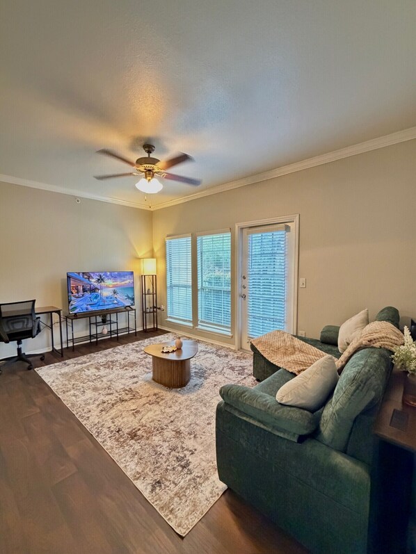 A living room with a green sofa, a coffee table, a TV, and a ceiling fan.