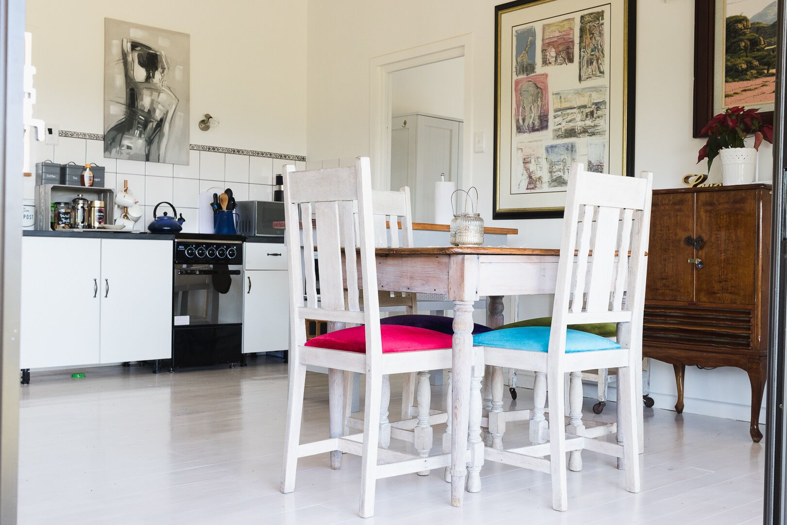 A kitchen with white cabinets, a stove, and a dining area with white chairs and a wooden table.