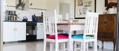 A kitchen with white cabinets, a stove, and a dining area with white chairs and a wooden table.