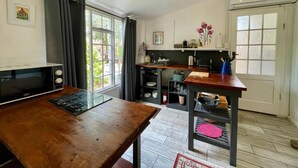 A compact kitchen with a microwave, a wooden table, and a window with curtains. - Equleni Farm (Knysna)