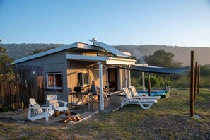 Una casa moderna con porche cubierto, mobiliario exterior y piscina.