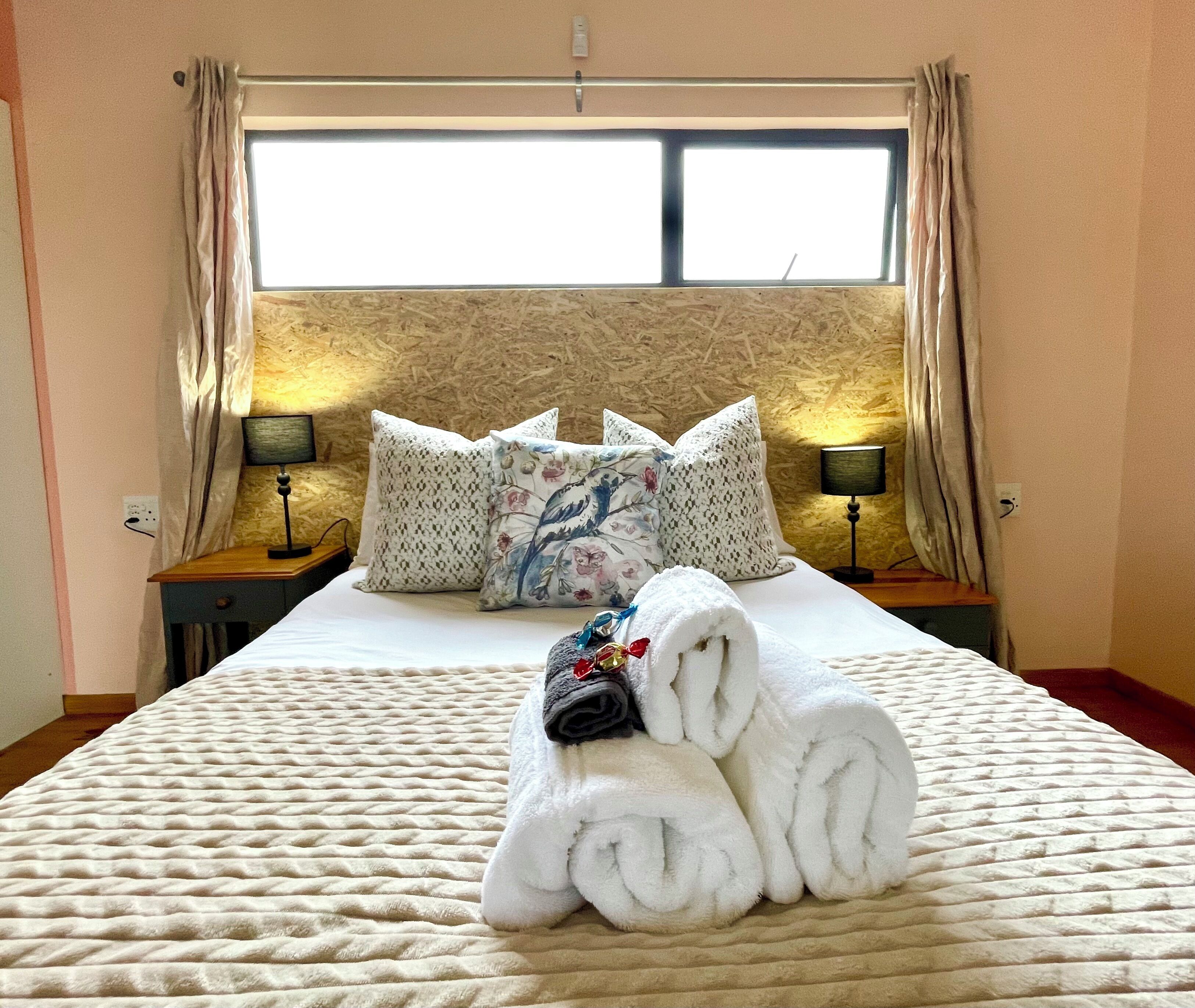 A hotel room with a bed, pillows, a lamp, and a towel arrangement.