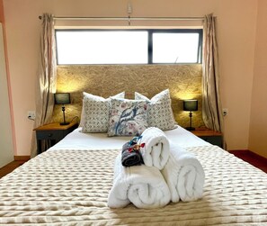 A hotel room with a bed, pillows, a lamp, and a towel arrangement. - Equleni Farm (Knysna)