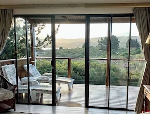 Una habitación con un amplio ventanal corredera que da a una terraza exterior con sillones y vistas a un paisaje boscoso.