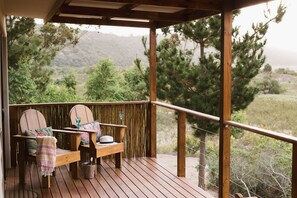 A wooden deck with two chairs and a table, a hat, and a glass on the table. - Equleni Farm (Knysna)