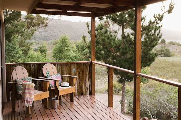 Una terraza de madera con dos sillas y una mesa, un sombrero y un vaso sobre la mesa.